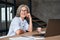 Smiling mature middle aged woman sitting at workplace with laptop, portrait.