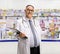 Smiling mature pharmacist standing with a clipboard in a pharmacy and welcoming