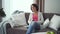 Smiling mature woman changing tv channel using remote sitting on sofa in home interior.