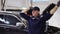 Smiling mechanic man in uniform and gloves dancing funny in a modern service auto center