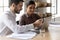 Smiling mentor teaching Indian businesswoman intern, pointing at laptop screen