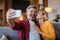 Smiling middle aged caucasian wife kisses husband on cheek, man with beard make selfie on smartphone