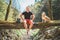 Smiling middle-aged man sitting on the fallen tree log over the mountain forest stream with his beagle dog while he waiting for