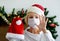 Smiling middle - aged woman in a medical mask and Santa hat. Remote congratulations on Christmas. Pandemic