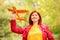 Smiling middle-aged woman standing in autumn park holding toy airplane and looking up in the sky. Power of dreams concept