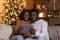 Smiling millennial black husband and wife have video call on tablet, watch video, sit on sofa in living room