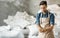 Smiling millennial brewery owner or worker in apron holds wheat or barley grains in hands in warehouse