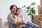 Smiling millennial european husband in glasses hugs wife in room interior with cardboard boxes with stuff