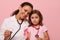 Smiling mixed race doctor and little girl, both with Breast Cancer Awareness pink ribbon and phonendoscope around their neck,