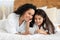 Smiling mom and little girl laying on bed, using smartphone