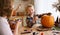 Smiling mother and child boy drawing scary faces on Halloween pumpkins while sitting in cozy kitchen