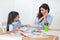 Smiling mother and daughter preparing for lessons and draws at the table with pencils and paints. Parent and pupil of preschool.