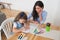 Smiling mother and daughter preparing for lessons and draws at the table with pencils and paints. Parent and pupil of preschool.