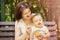 Smiling mother feeding child with pumpkin puree on bench outdoor. Kid does not want to eat, baby is turning face away from spoon