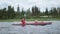 Smiling mother happy raises paddle above head and rows bright orange sports kayak with little kid sailing along lake