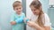 Smiling mother having fun with her toddler son while putting on protective rubber gloves before cleaning and washing