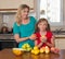 Smiling mother and her keeping sweet pear daughter. Healthy eating - woman and child in the kitchen with different kinds of fruits