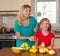 Smiling mother with keeping sweet pear daughter. Healthy eating - woman and child in the kitchen with different kinds of fruits