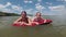 Smiling mother and little daughter float together on a red air mattress on the water far from the shore. They look at