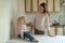 Smiling mother looking at little daughter at table in kitchen. Morning breakfast