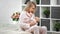 Smiling mother nursing cute toddler sitting on bed in cozy white bedroom. Medium shot on RED camera