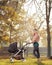 A smiling mother posing with a baby stroller in a park in autumn