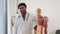 Smiling multicultural male adult in lab wearing lab coat and stethoscope embracing anatomy skeleton