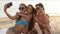 Smiling multiracial friends sitting together on towel on white sand beach during their vacation in an idyllic nature