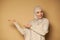 Smiling Muslim woman with covered head in hijab points side on beige background with copy space