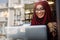 Smiling muslim woman using laptop at cafe