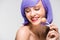 Smiling naked girl in purple wig holding sweet lollipop