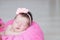 Smiling newborn sleeping in basket with knitted flower on head, baby girl lying on pink blanket, cute child