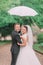 The smiling newlyweds under the white umbrella spending their time in the park.