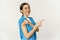 Smiling nurse, female healthcare worker in scrubs, pointing finger right, showing patch on shoulder, vaccination