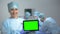 Smiling nurse holding tablet PC with green screen during operation, hospital ad