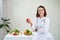 Smiling nutritionist in her office, she is holding a green apple and showing healthy vegetables and fruits, healthcare and diet