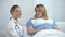 Smiling obstetrician and pregnant female holding tummy looking at camera