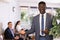 Smiling office employee African man stands in reception area and enjoys successful good day.