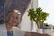 Smiling old woman near the window. Happy senior woman sitting near window with flowers.