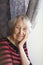 Smiling old woman near the window. Happy senior woman sitting near window with flowers.