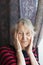 Smiling old woman near the window. Happy senior woman sitting near window with flowers.