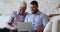 Smiling older father his son sit on sofa use laptop