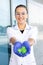 Smiling oriental female scientist in a white coat, goggles, and rubber gloves showing green molecules in hands