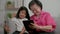 Smiling overjoyed mature grandmother with little granddaughter using tablet on cozy couch. Happy mature granny and small