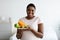 Smiling overweight African American woman holding plate of fresh fruits, keeping healthy diet for weight loss at home