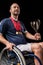 Smiling paralympic in wheelchair with gold medals on neck holding champion goblet