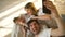 Smiling parents with baby taking selfie family photo on bed at home