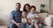 Smiling parents two children sit on sofa look at camera