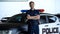 Smiling patrolman standing near car with crossed hands, carrying out duties