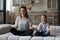 Smiling peaceful mom and daughter meditating at home